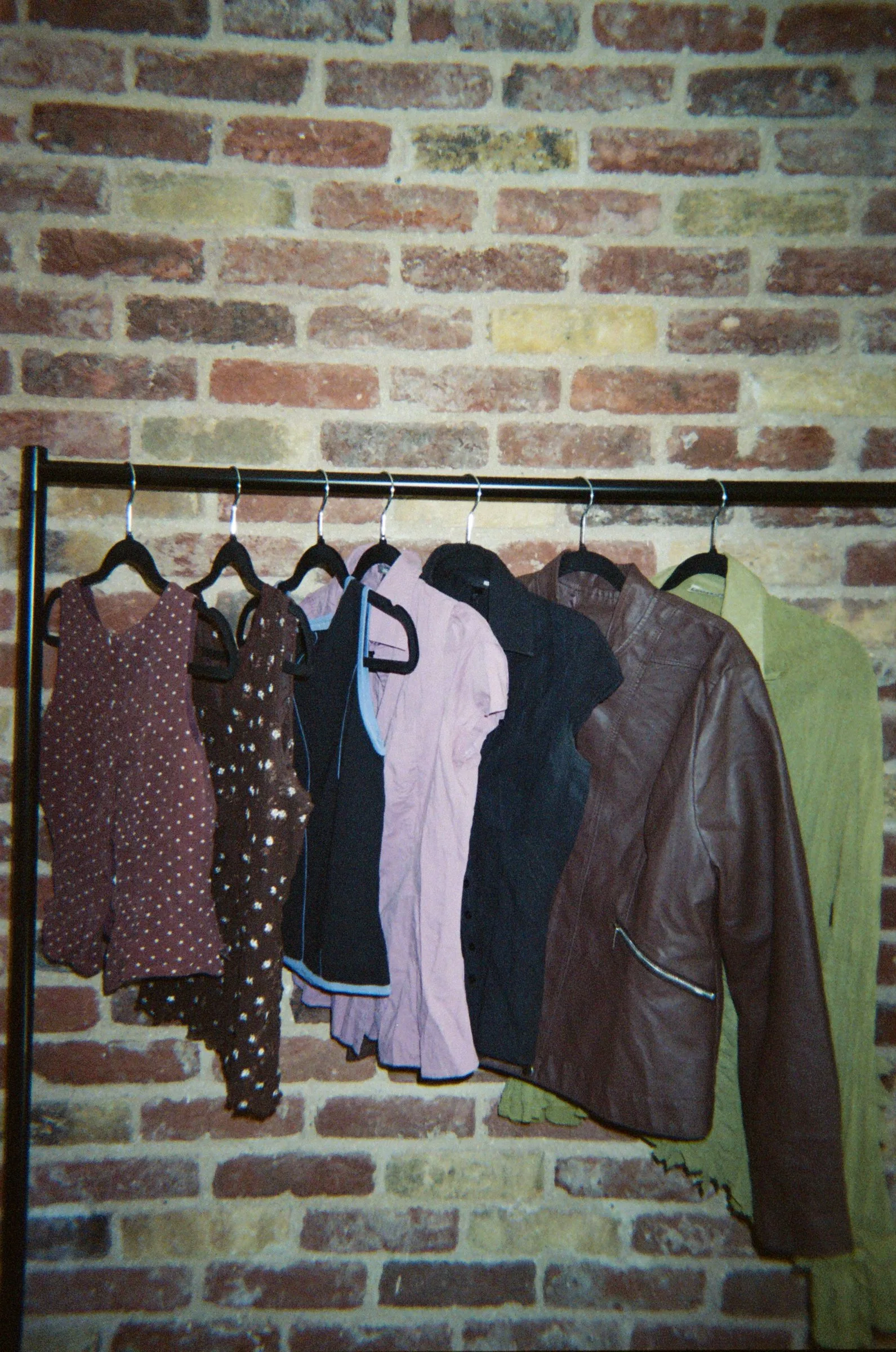 A rail of coats and dresses hanging against a bare brick wall