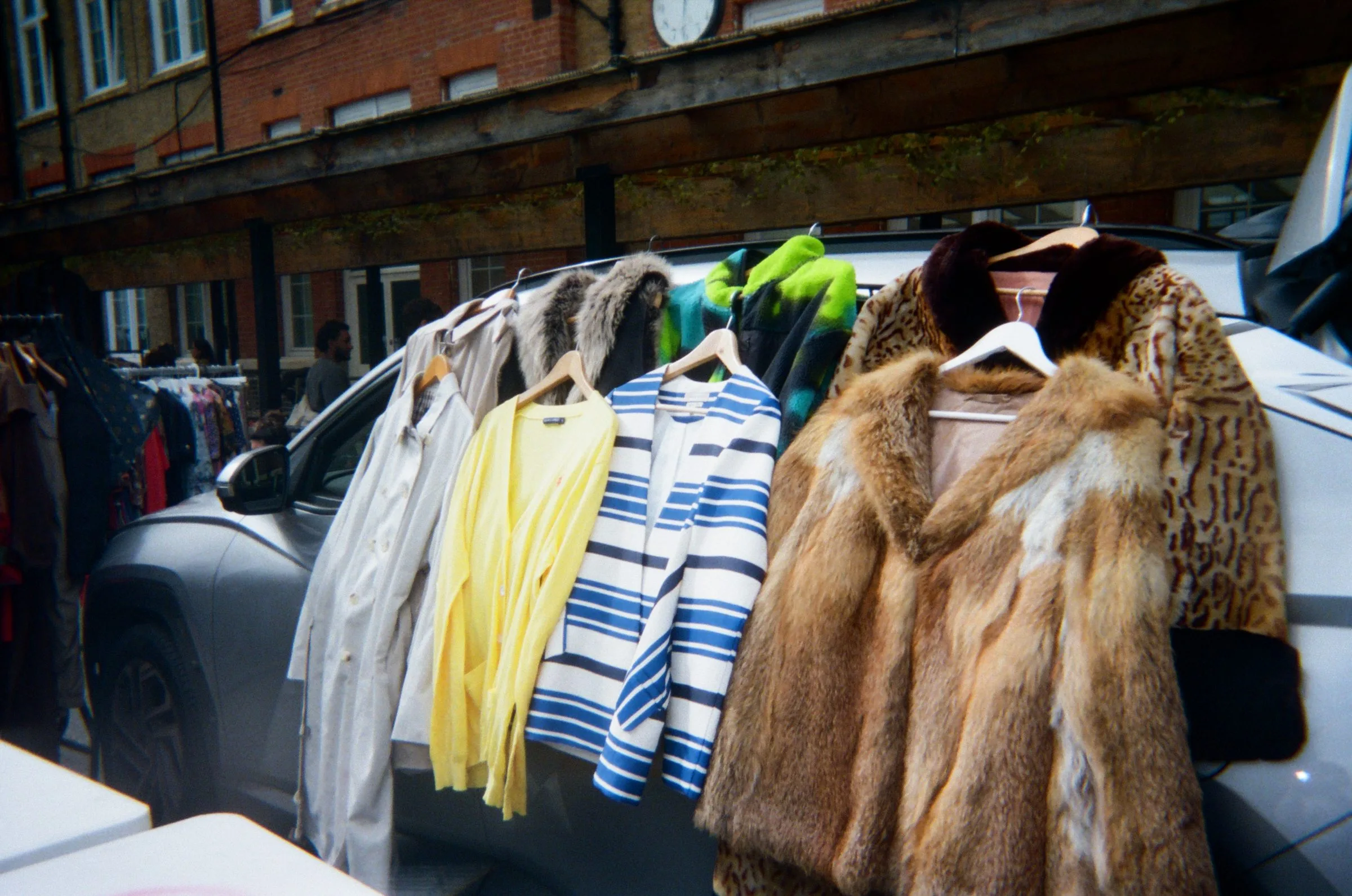 Fur coats and knitwear hanging on a rail beside a van at a market