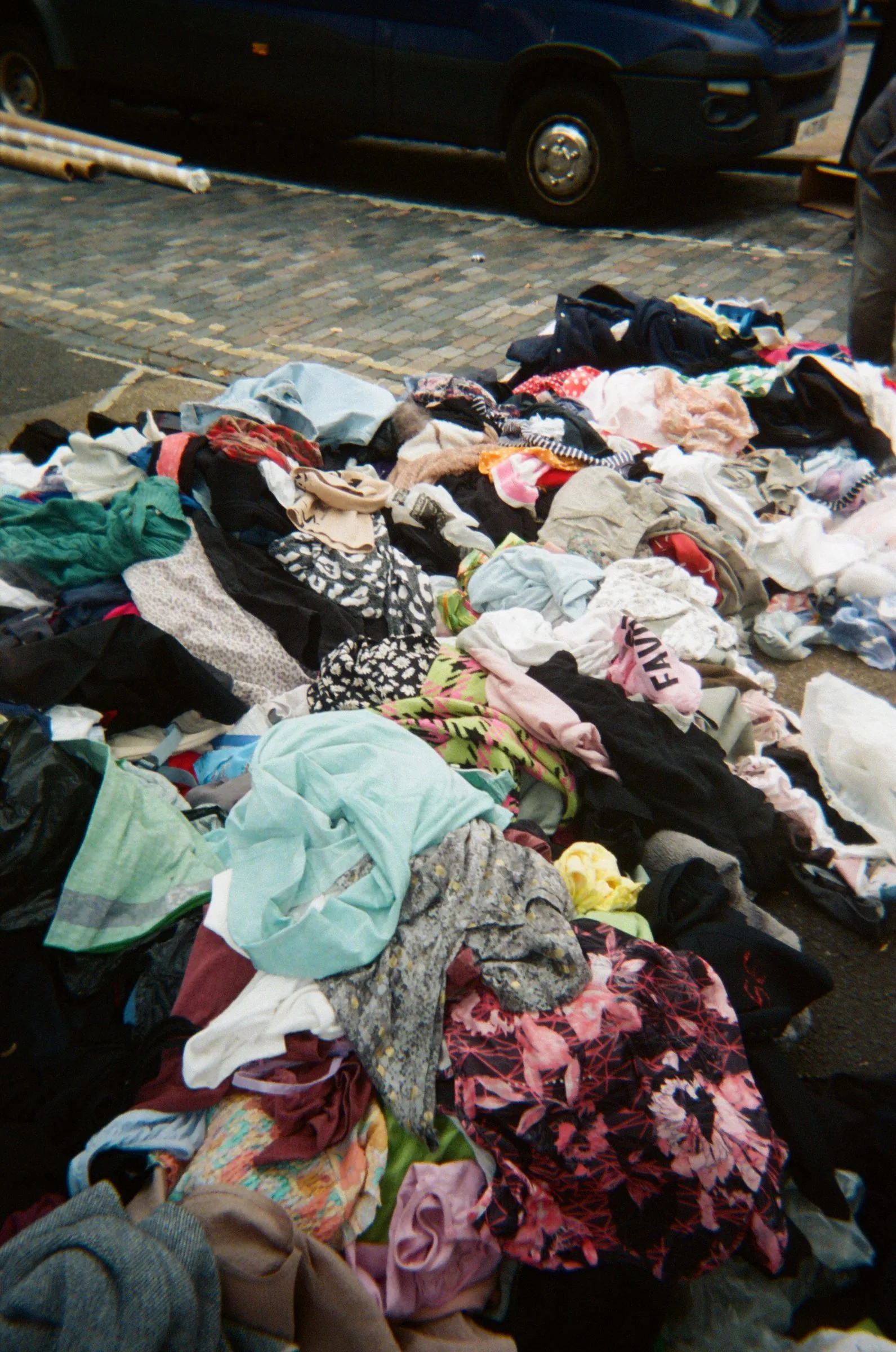 Clothes spread out across a cobbled street beside a parked van