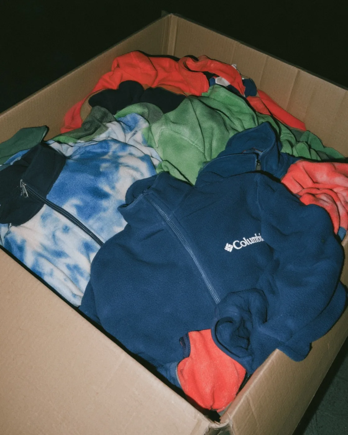Columbia and other fleece jackets piled in a cardboard crate