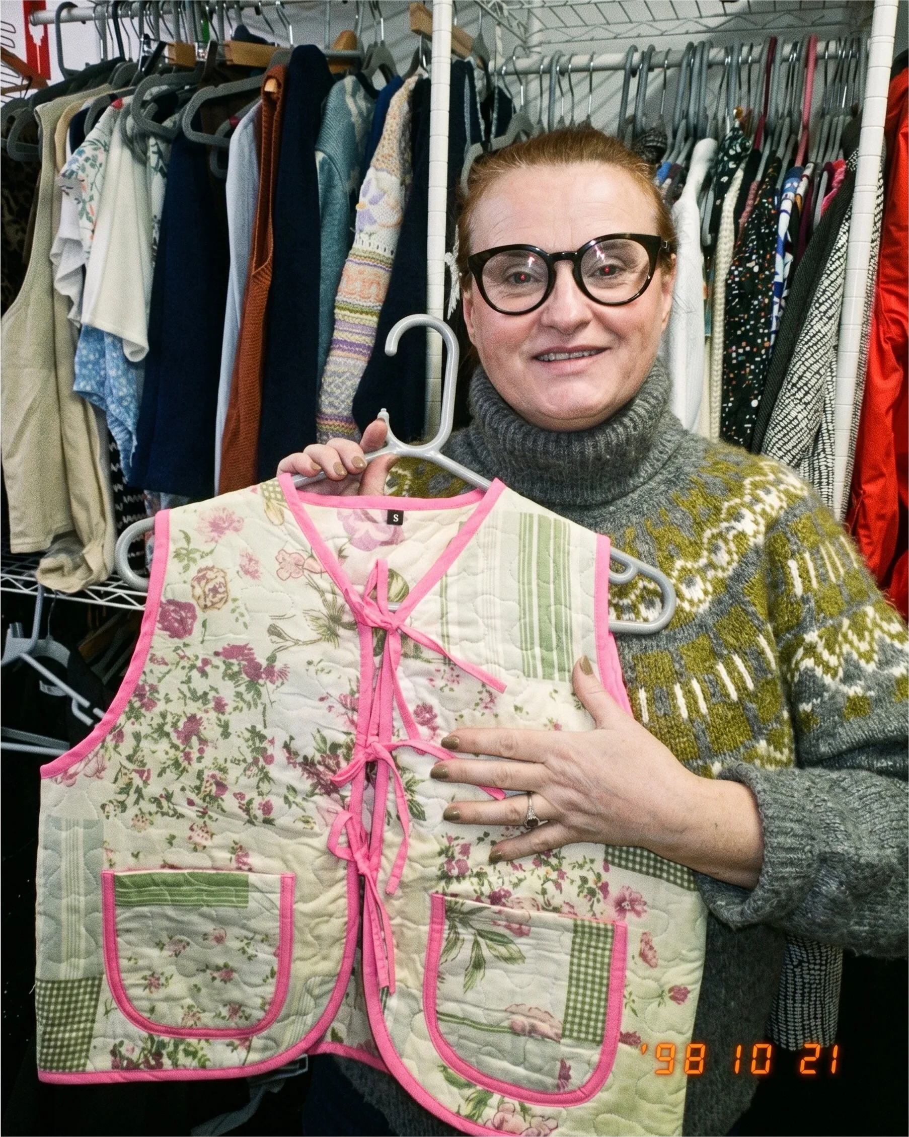 A reseller holding up a floral quilted waistcoat in a charity shop