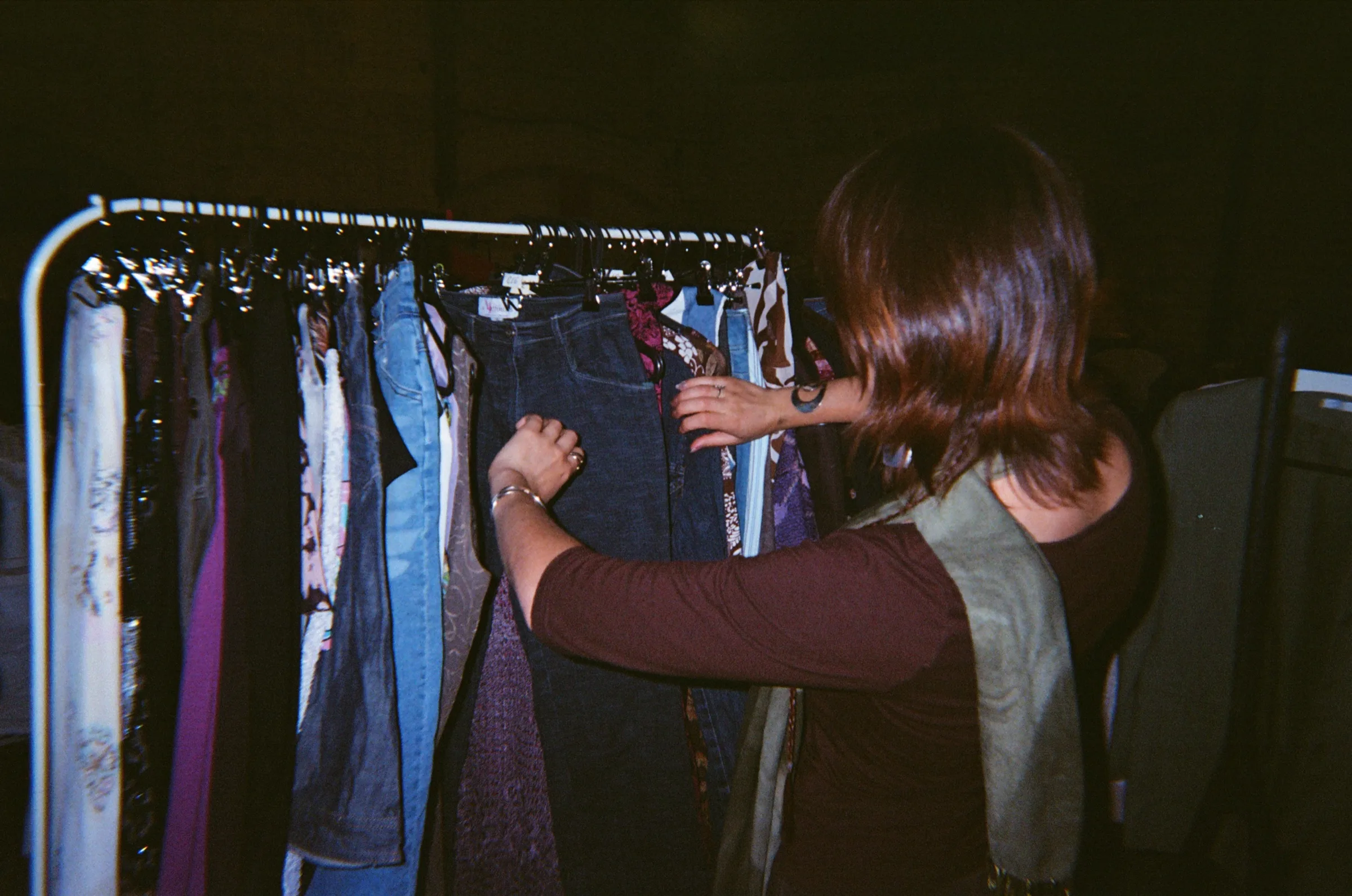 A reseller pulling a pair of jeans from a packed rail at a vintage market