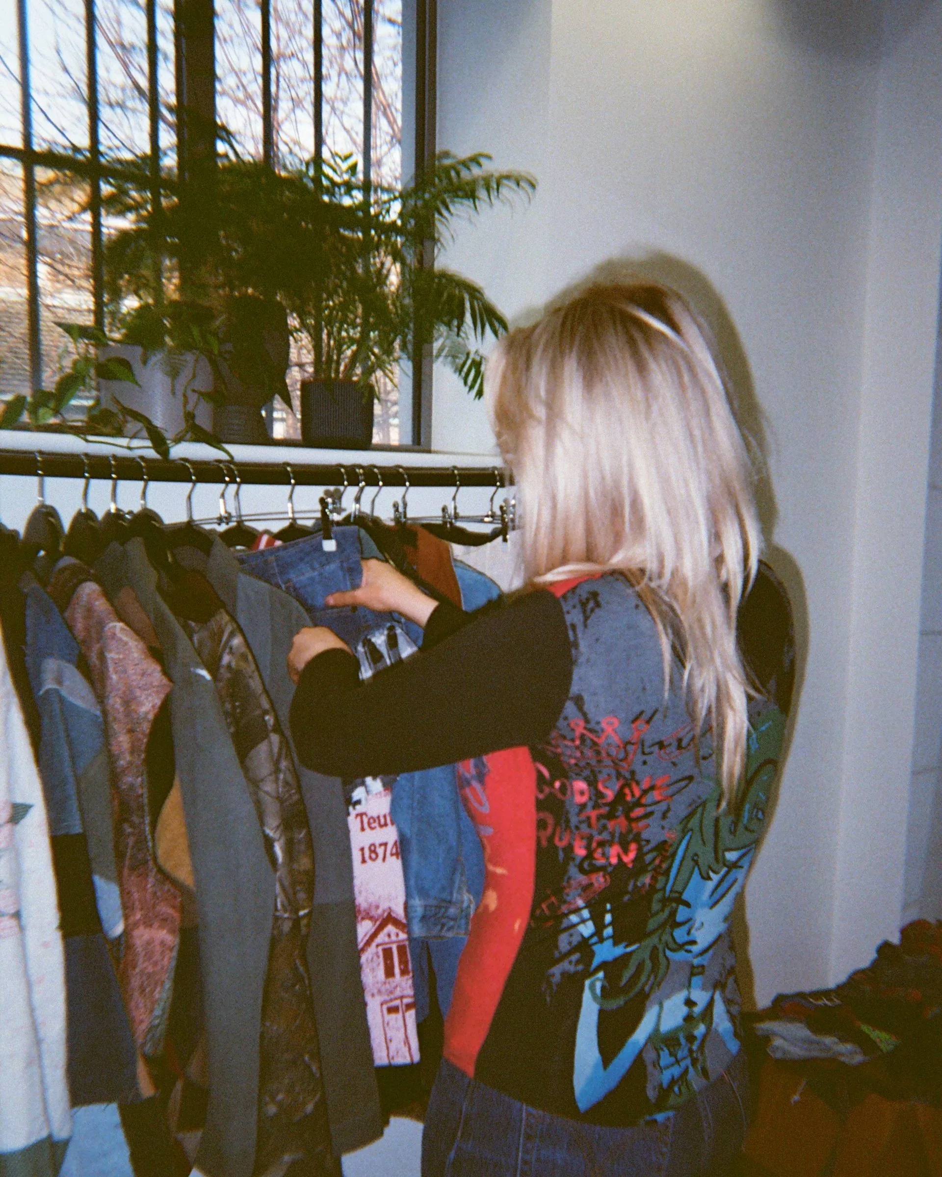A reseller pulling a denim jacket from a rail beside a window