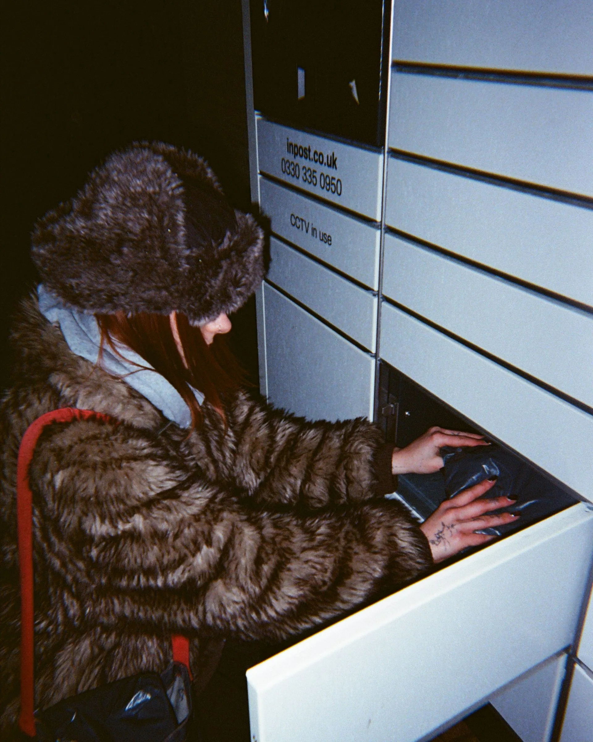 A reseller in a fur coat posting a parcel into a locker at night