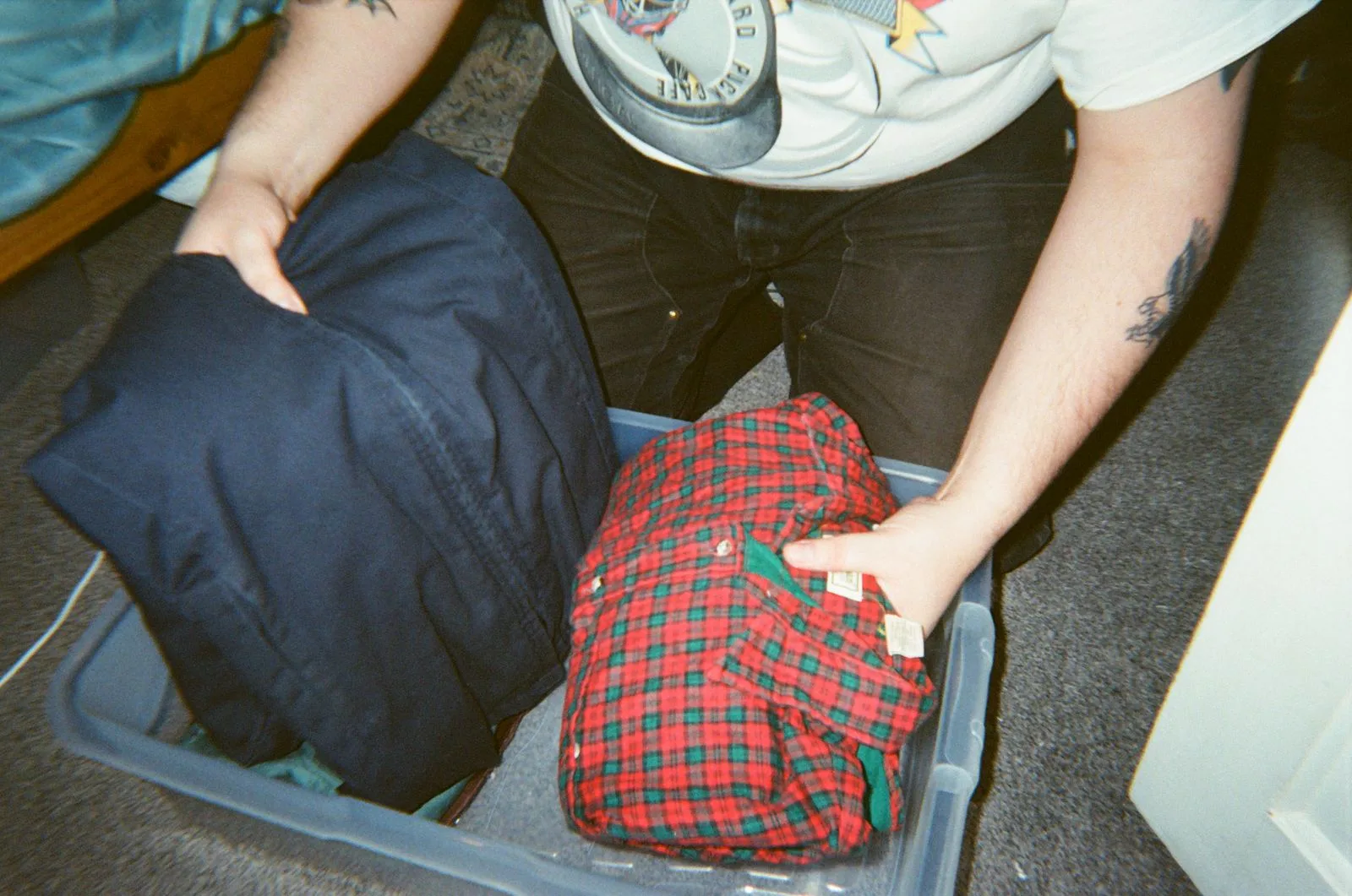 Hands packing folded shirts into a plastic storage tub
